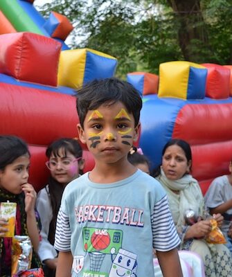 A child with his face painted stands in front of a party inflatable